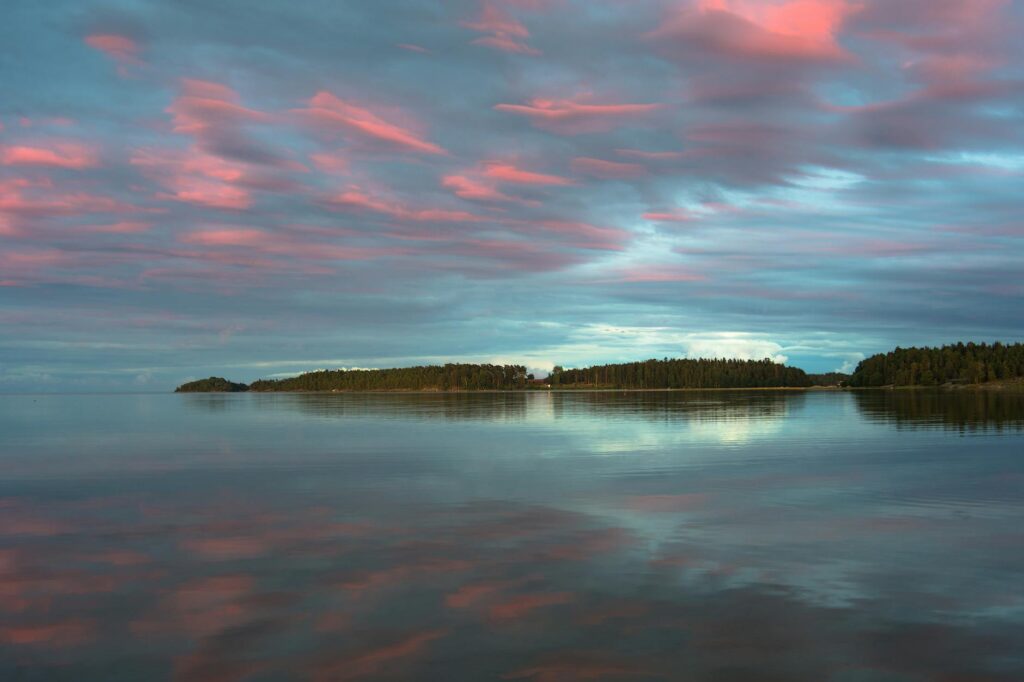 Serene sunset over a lake with pink clouds reflecting on the water, creating a peaceful scene.