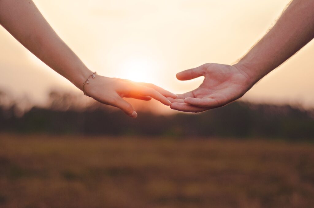 Crop anonymous female with bracelet touching hand of unrecognizable male in field against sundown