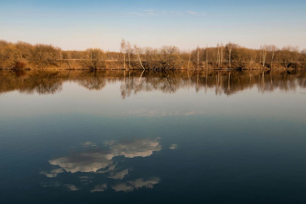 Peaceful lake landscape with trees and clouds reflecting on the water during sunset.
