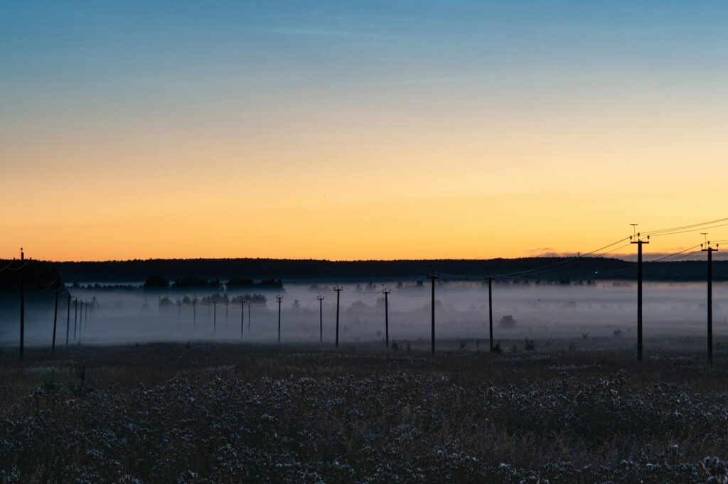 Misty morning sunrise over a grass field with electric posts, creating a serene and tranquil landscape.