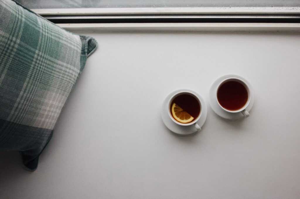 A serene still life of two cups of tea on a windowsill with a plaid pillow, capturing a cozy moment indoors.